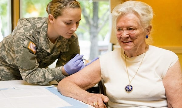 Woman in military uniform giving shot to woman.