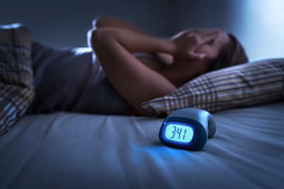 Woman lying in bed with her hands on her head.